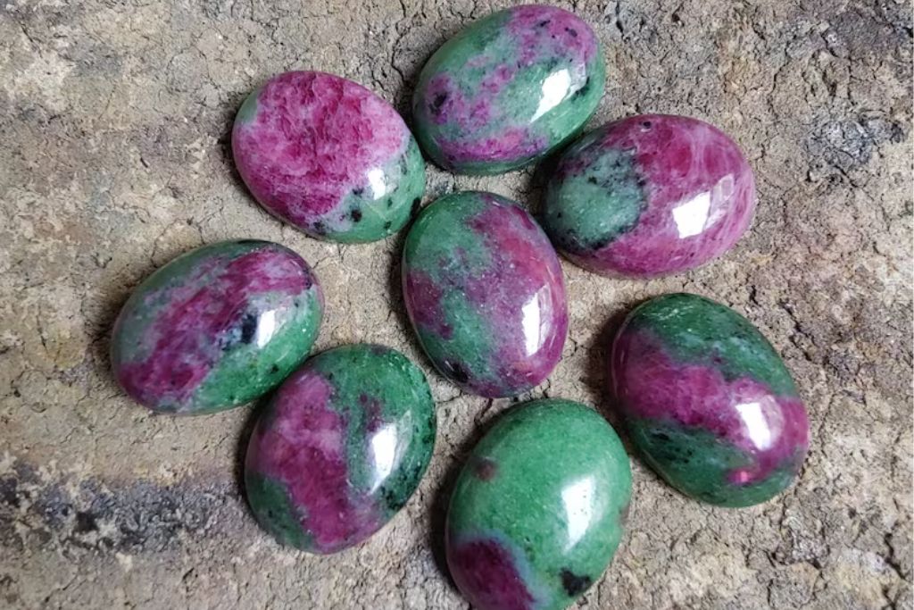 8 pieces of polished oval shaped Ruby Zoisite placed on the ground