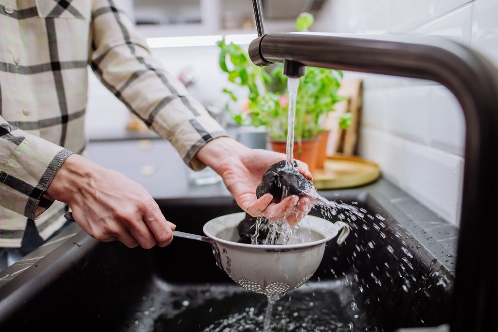 woman cleaning Shungite stones in sieve with pouring water in sink