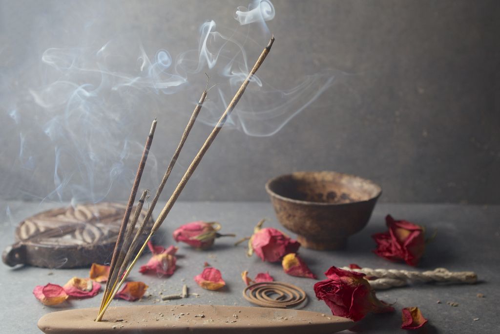 4 sticks of burning incense in an incense wood stand with flower petals scattered around it