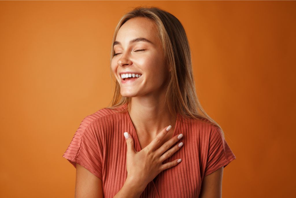 a happy woman holding her chest with her right hand on orange background