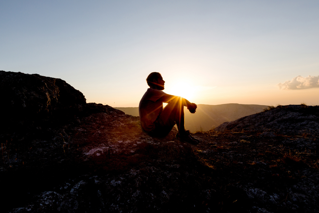 man sitting on the ground in a mountain looking away