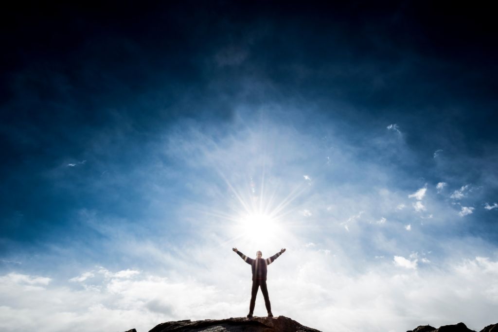 A man standing on a rock lifting his arms up on a sky background
