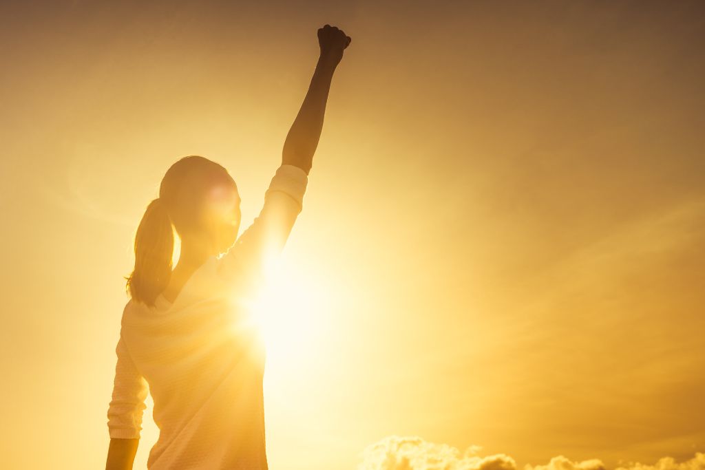 woman raising her right hand fist close on a sunset background