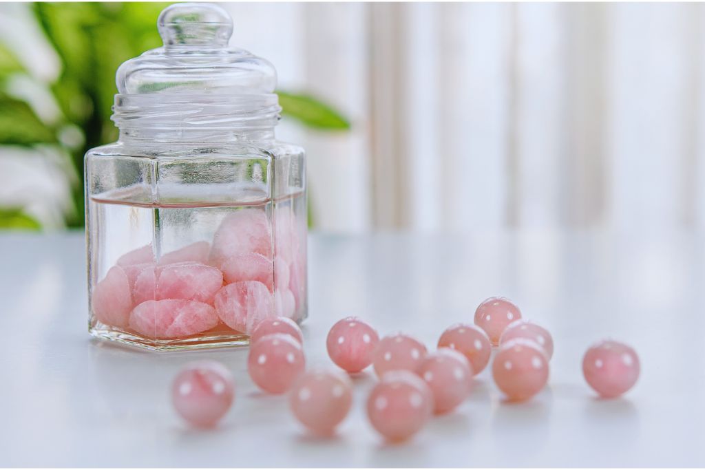 A glass jar with chunks of Rose Quartz submerged in water is placed on the table.