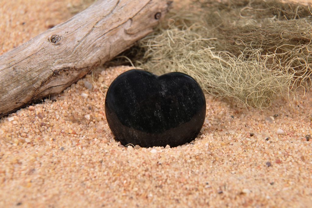A heart shape black Obsidian crystal on a sand