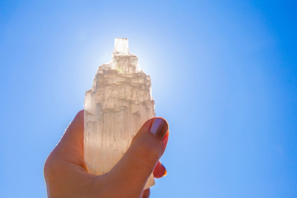 A person is holding a selenite crystal under the sunlight
