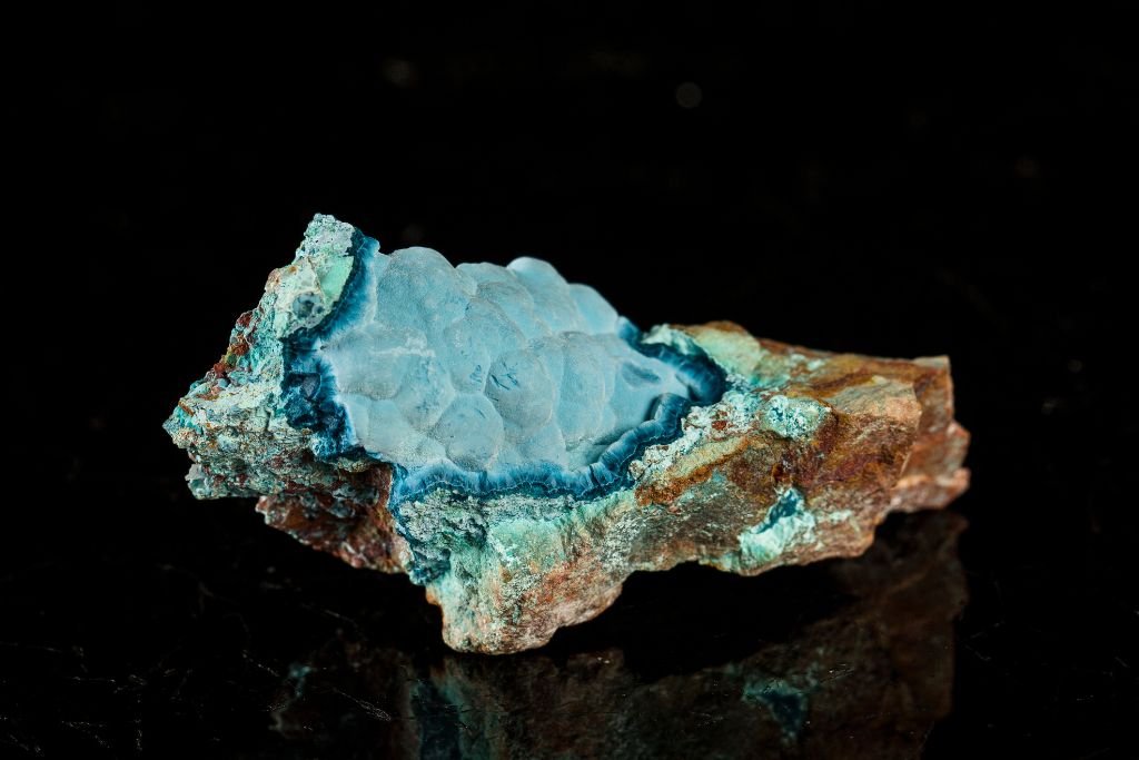 A raw Shattuckite crystal on a black reflective background