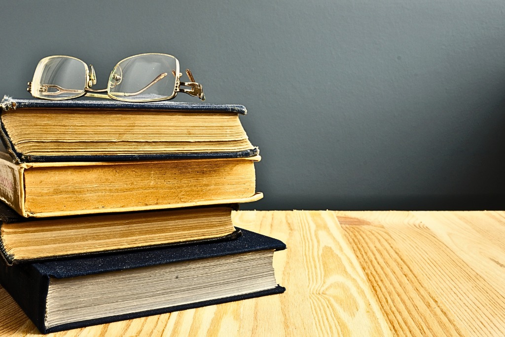 A stack of books and a pair of eyeglasses are on top of it.