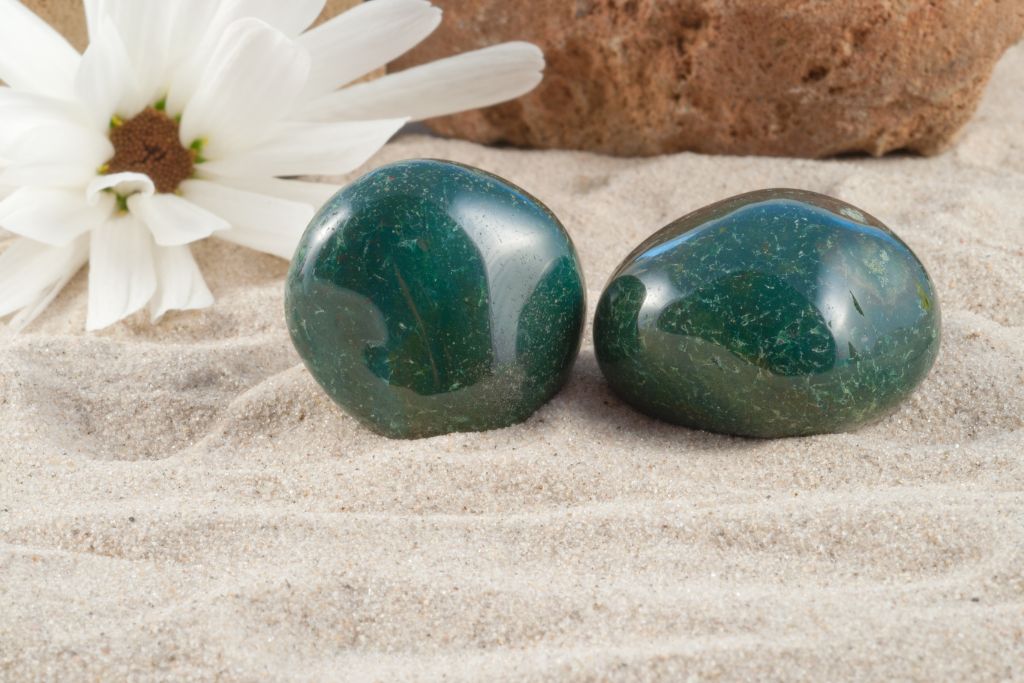 2 polished bloodstone on a white sand beside a flower