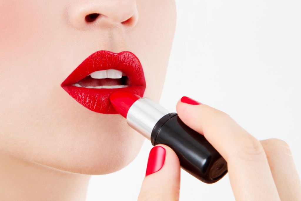 close up look of a woman applying red lipstick on a white background