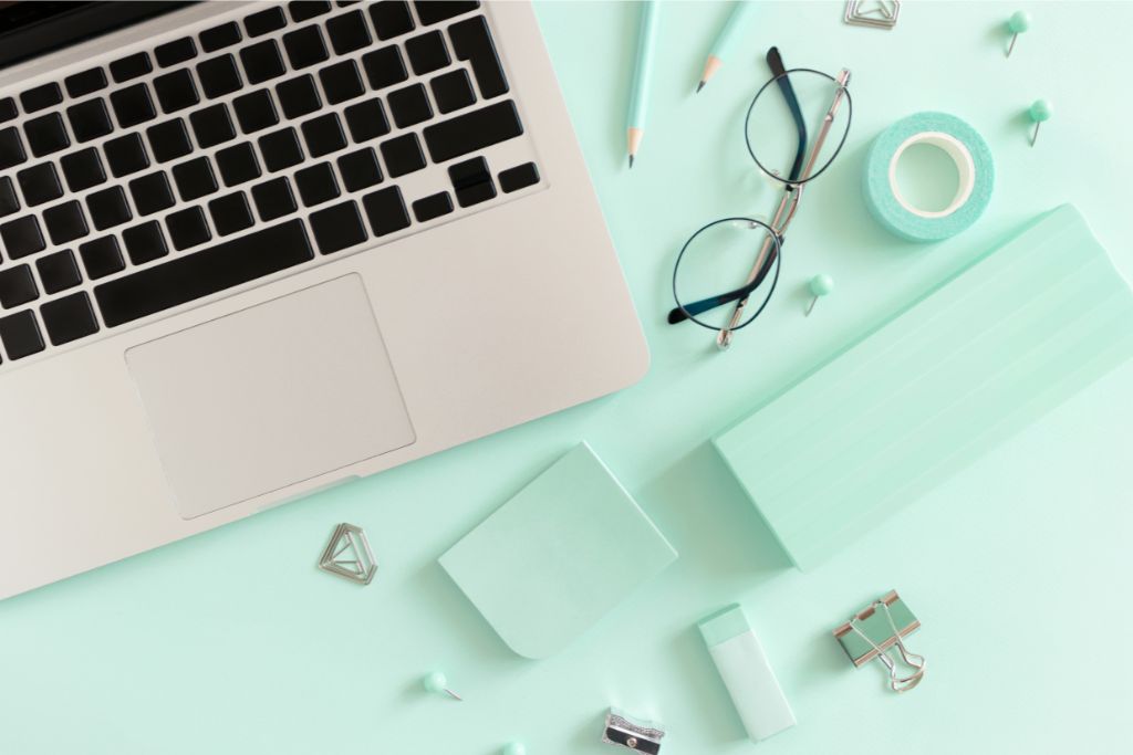 A laptop and eyeglasses on a mint green table