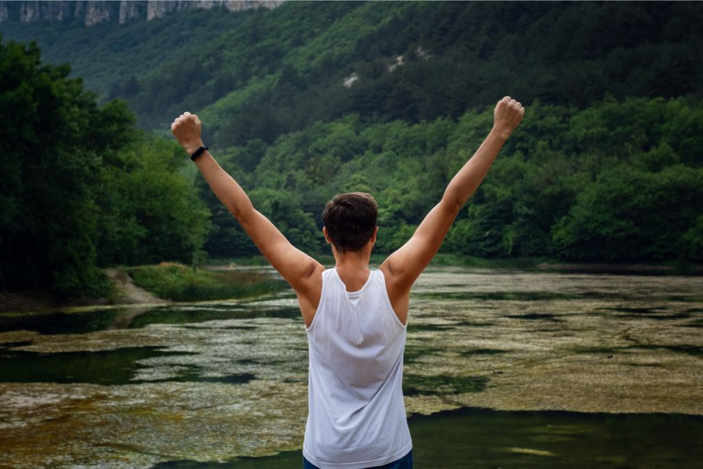 A man beside a lake raising his arms. 