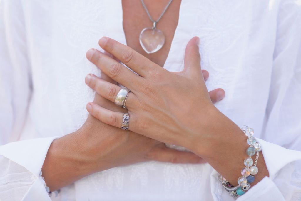 Spiritual woman wearing crystal necklaces, bracelets, and rings touching her chest with two hands. 