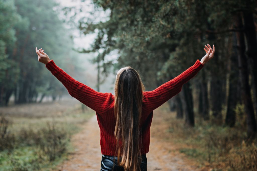 a woman lifting her hands up while looking at the sky in the forest