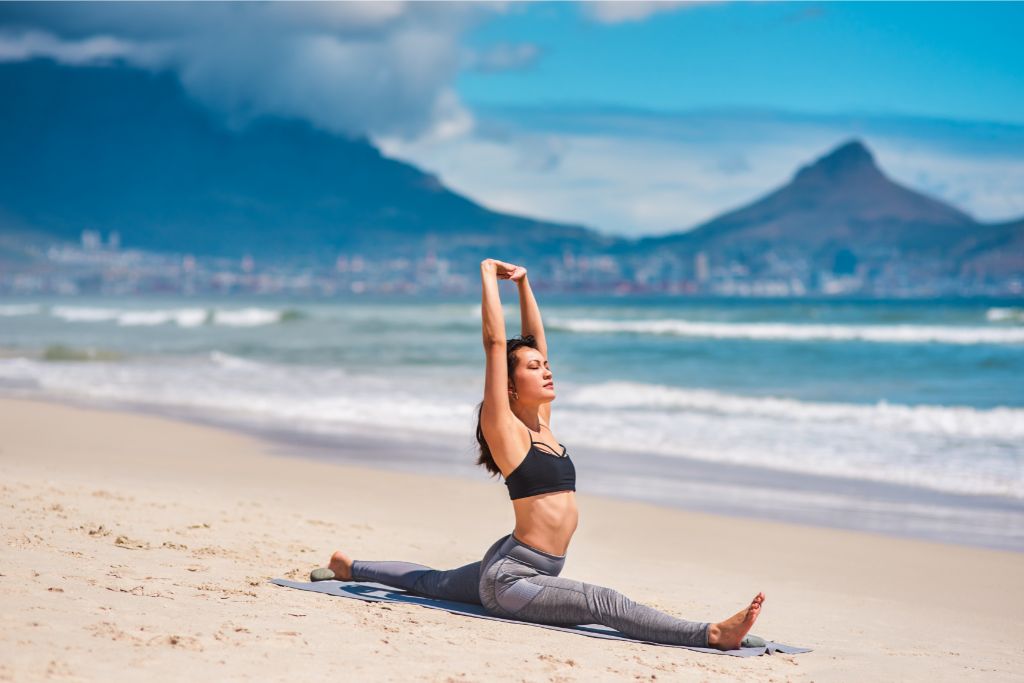 a woman doing yoga beside the shore on a sunny day