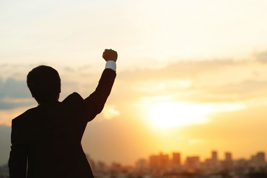 A man raising his fist while looking at a sunset.