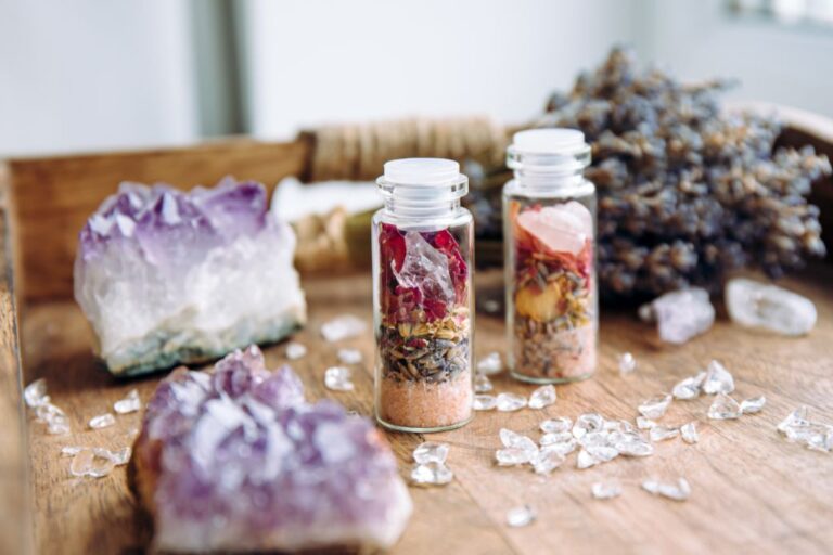 An amethyst crystal, lavender flowers, and 2 jars with crystals and stuffs inside on a table.