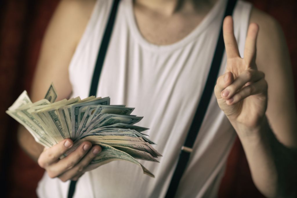 A person holding money on his right hand while making peace sign on his left hand