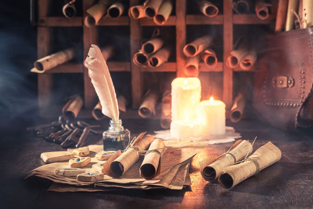 Rolled ancient papers, two lit candles, and quill pens and ink. 