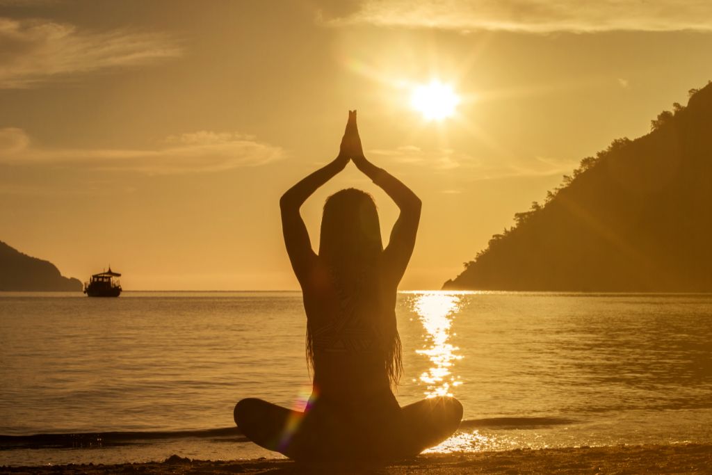 meditating woman under sunset by the ocean