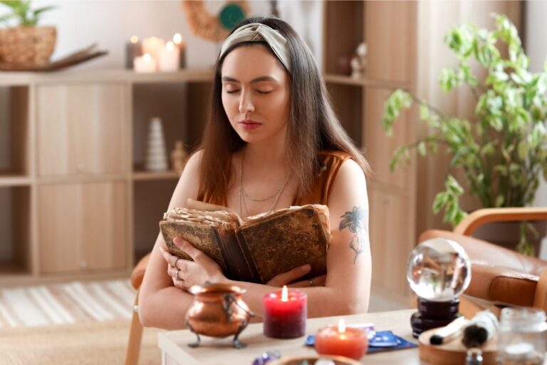 A young woman stands before a table lit by candles, her eyes closed as she reads from a spell book