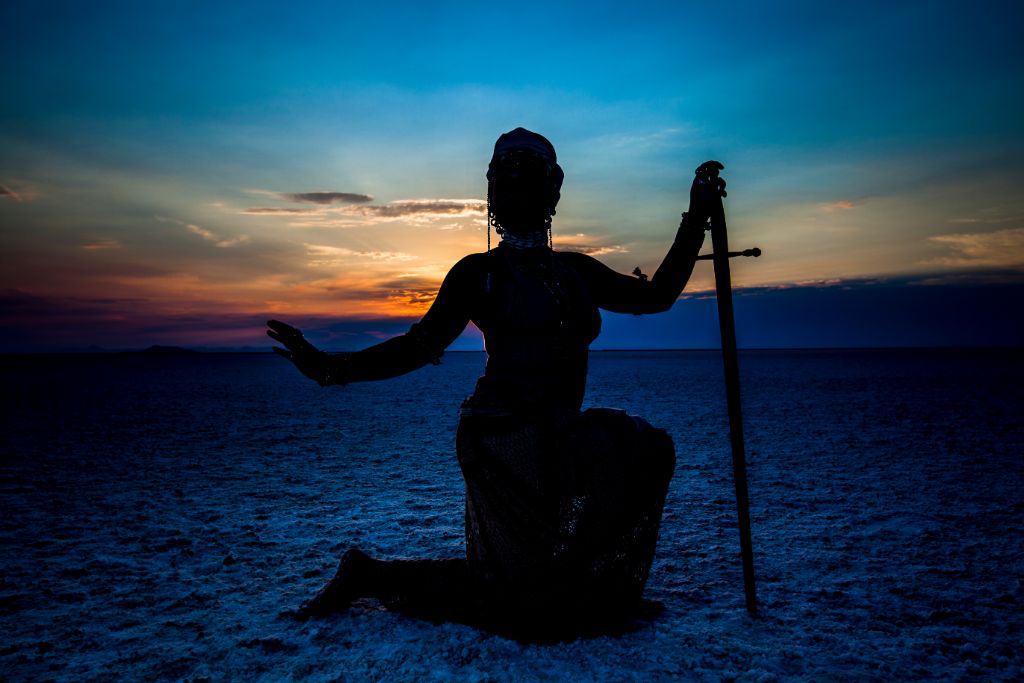 woman holding a sword and kneeling on the sand depicting divine feminine