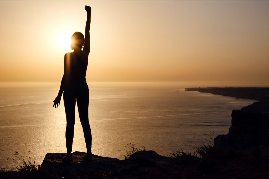 woman raising her hand on a cliff depicting empowerment