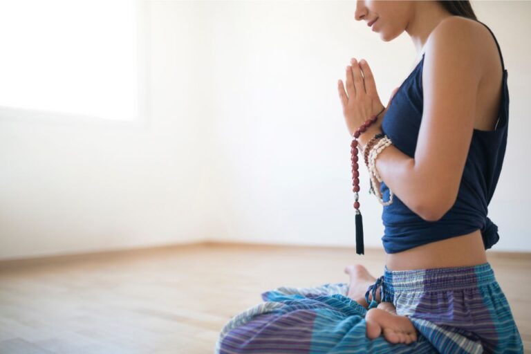 girl sitting with her hands in prayer position, holding a string of beads depicting mantra