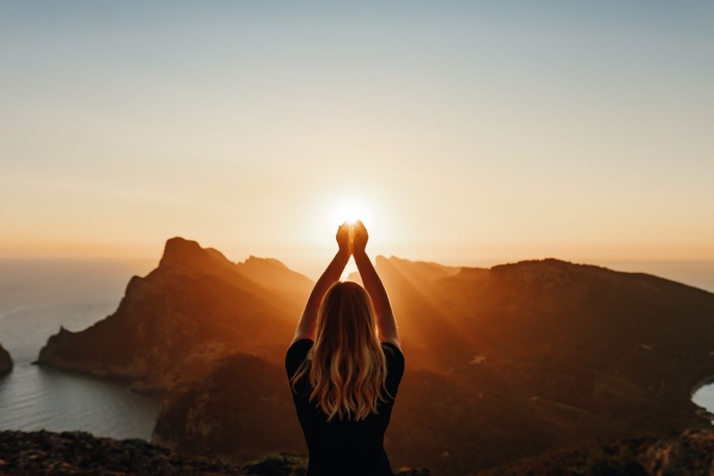 girl holding her hand up while facing the sunrise depicting spiritual expansion