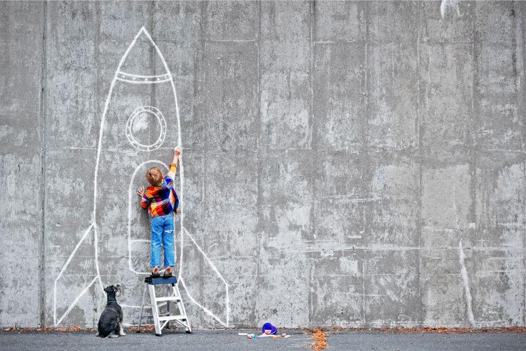little boy drawing a rocket on a wall depicting dreaming big