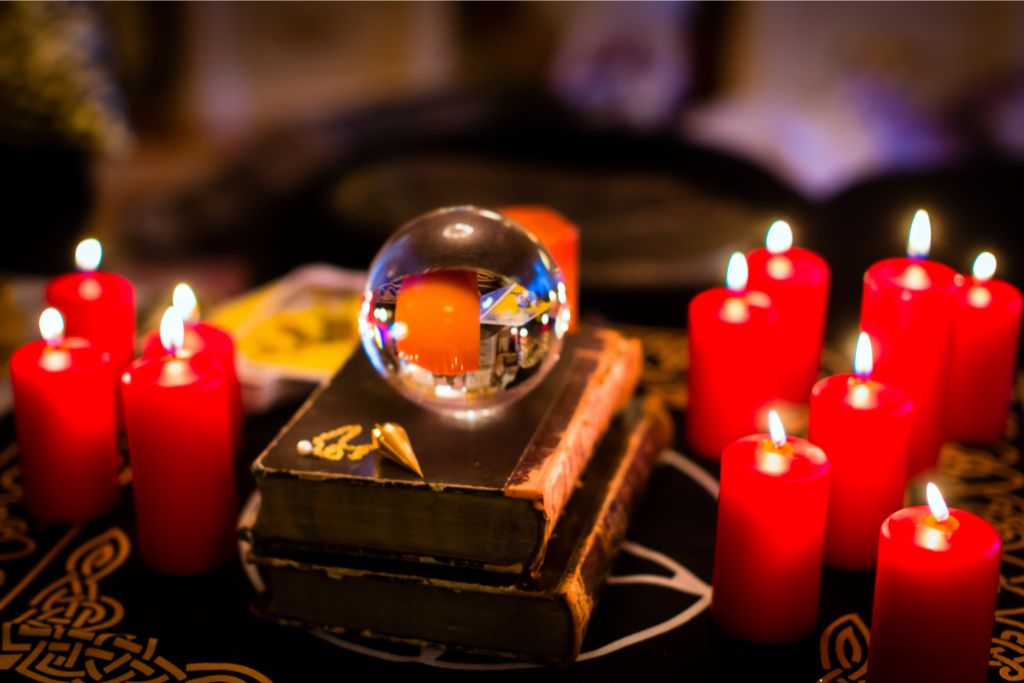a crystal ball under books and surrounded by red candles