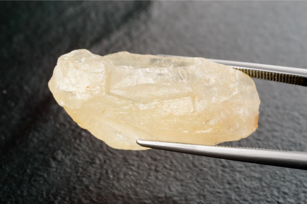 Calcite held by tweezer over black stone