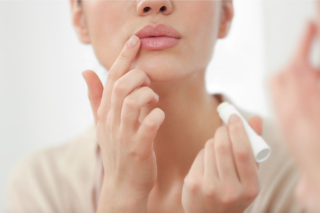 woman applying lip gloss in front of a mirror