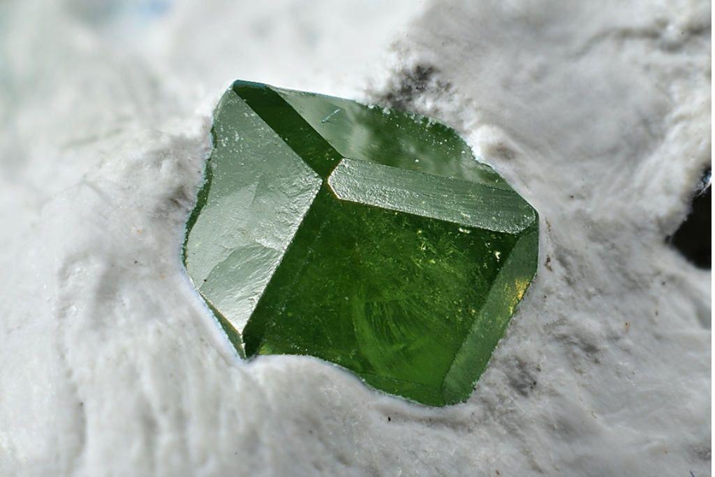 Vibrant green Andradite crystal resting on a white mineral base.